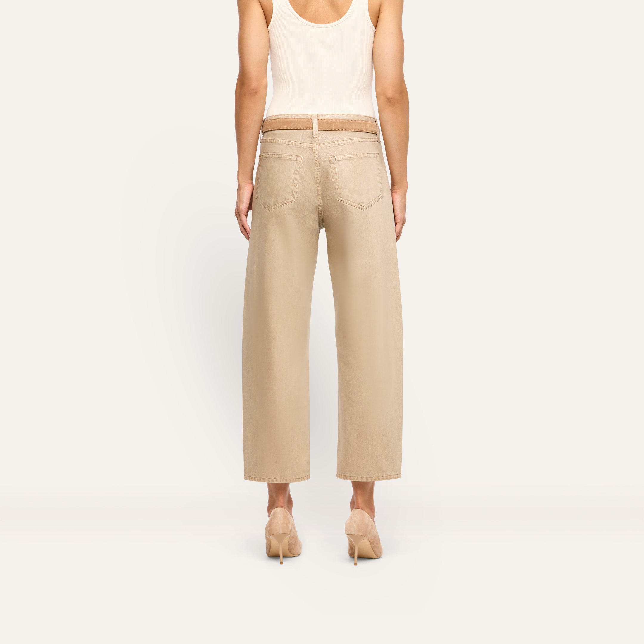 Back view of a person wearing Mallis Coated Bow-Leg Jean in beige, featuring a high-rise, wide-leg cut with a thin belt and pointed-toe heels.