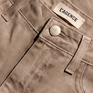 Close-up of the waistband of tan Mallis Coated Bow-Leg Jean high-rise, wide-leg jeans, featuring a metal button and a brand label.