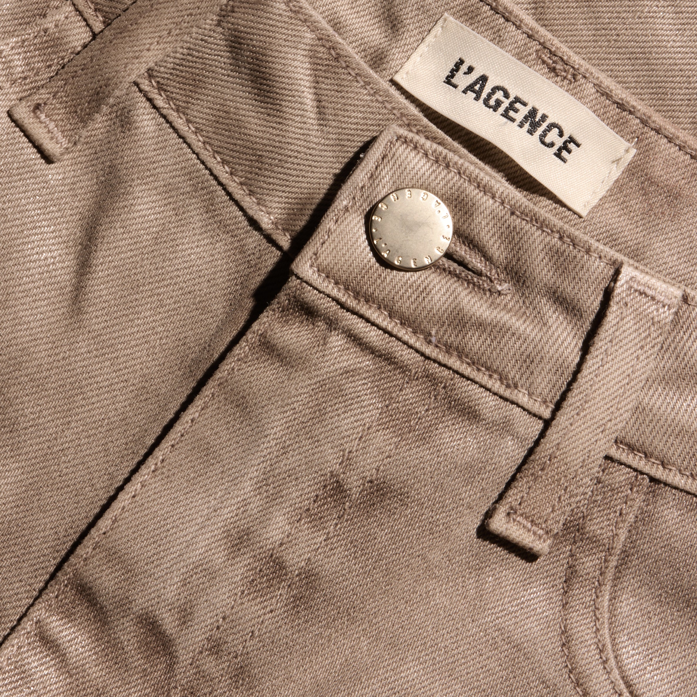 Close-up of the waistband of tan Mallis Coated Bow-Leg Jean high-rise, wide-leg jeans, featuring a metal button and a brand label.