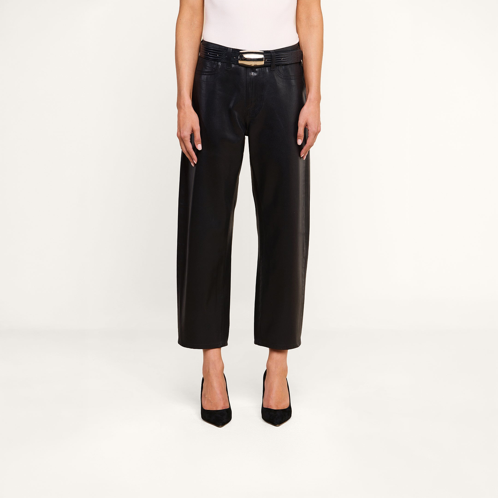 베이지색 배경 앞에, 블랙 컬러의 ‘Mallis Coated Bow-Leg Jean’을 입고, 골드 버클이 달린 블랙 벨트와 화이트 민소매 상의, 블랙 뾰족한 앞코 힐을 매치한 한 사람이 서 있다.