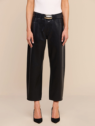 A person wearing the Mallis Coated Bow-Leg Jean in black, styled with a black belt featuring a gold buckle, a white sleeveless top, and black pointed-toe heels stands against a beige background.