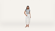 A woman wearing a floral top, white pants, and sandals stands facing forward against a plain white background.