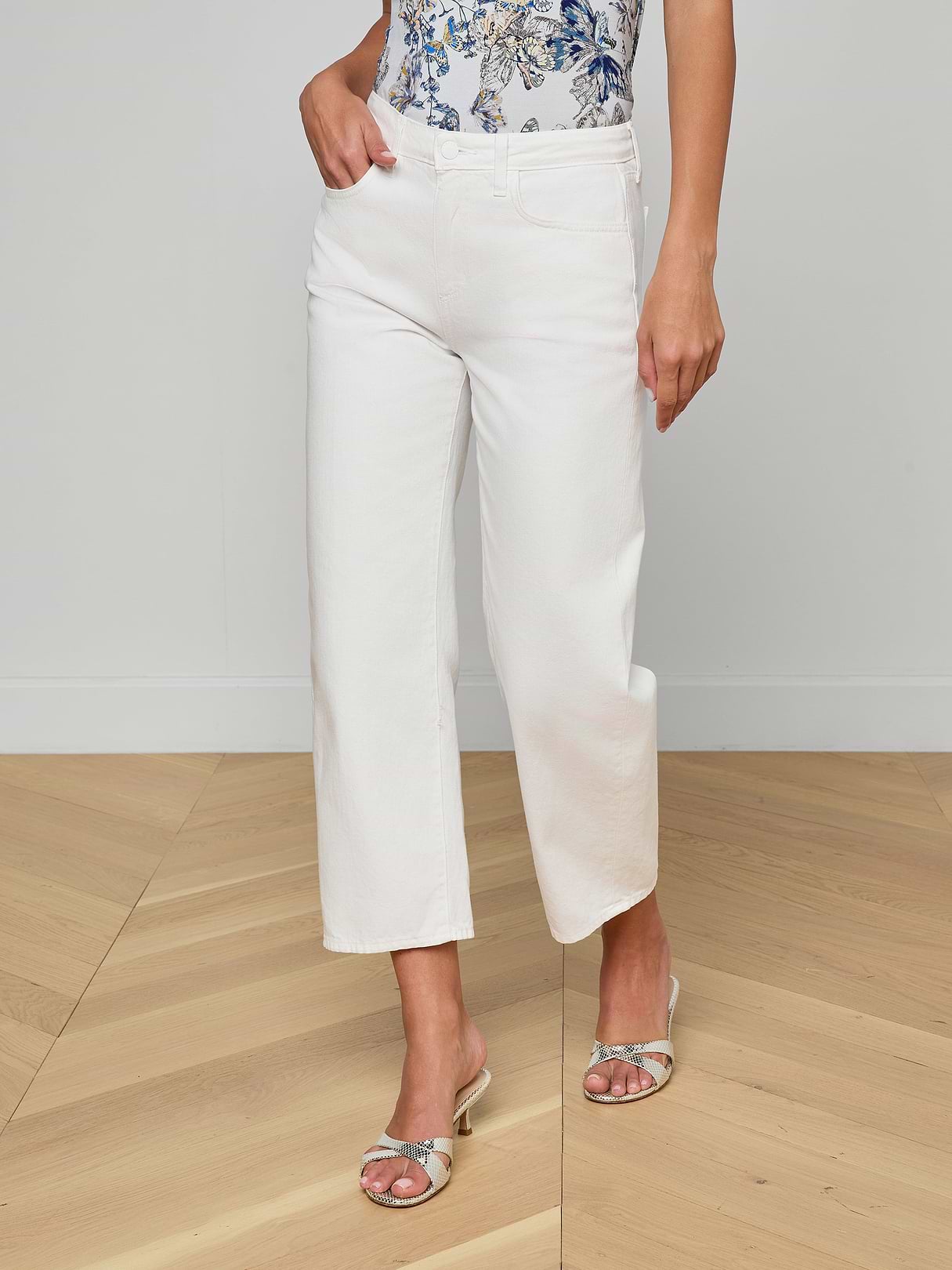 Person wearing white pants and a floral top on a wooden floor.
