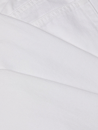 Close-up of overlapping pieces of white all-cotton denim fabric from the Mallis Bow-Leg Jean, showcasing visible stitching and texture.