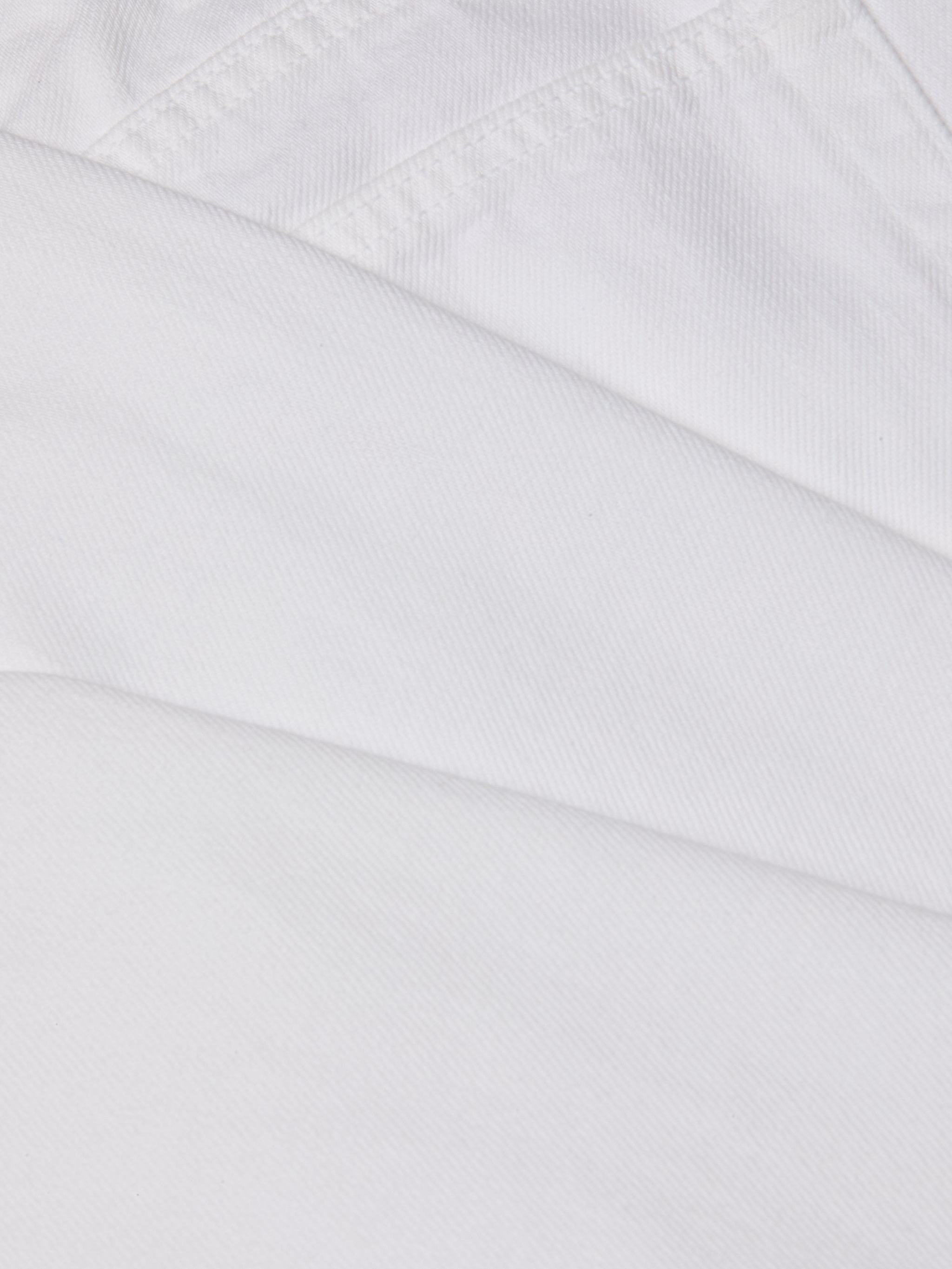 Close-up of overlapping pieces of white all-cotton denim fabric from the Mallis Bow-Leg Jean, showcasing visible stitching and texture.
