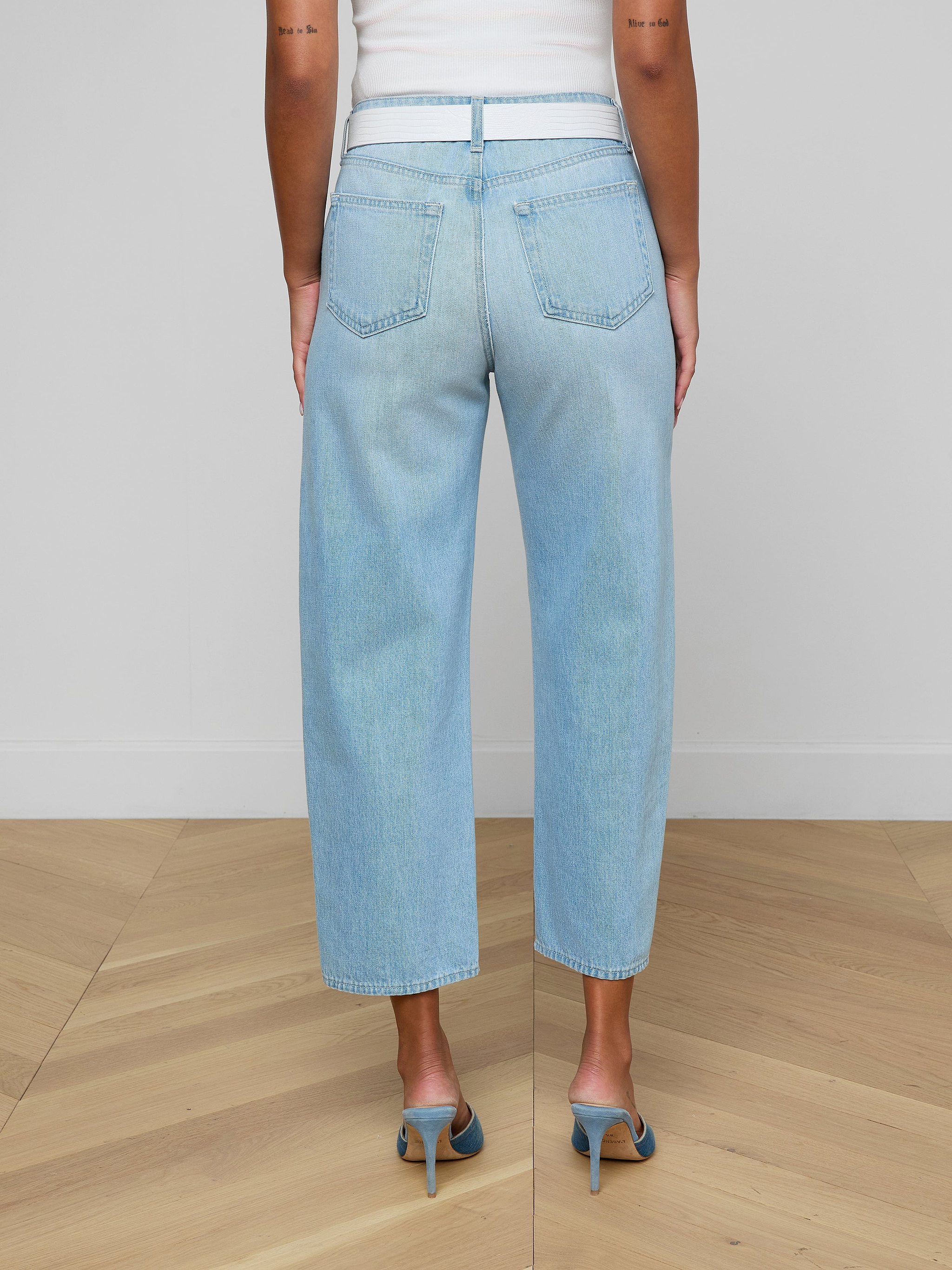 A person wearing the Mallis Bow-Leg Jean in a light wash and high heels stands with their back to the camera against a plain white background.
