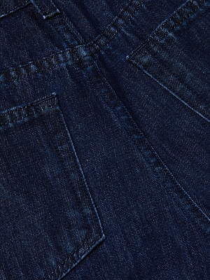 Close-up of dark blue denim fabric highlighting the stitching and back pockets of the Mallis Bow-Leg Jean. The texture and weave of this high rise jean are clearly visible.