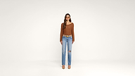 Woman stands facing forward against a plain white background, wearing a brown long-sleeve top, blue ripped jeans, tan heels, a tan belt, and sunglasses. Her hair is straight and loose.