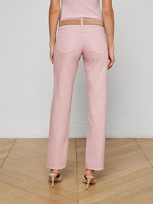 A person stands with their back turned, wearing the Armida Low-Rise Slouch Jean in light pink, a matching top, and beige heels on a wooden floor with a plain white wall behind them.