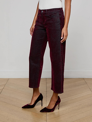 A person wearing L’AGENCE Dolores Flocked Bow-Leg Jean in bordeaux, a white top, and matching burgundy heels stands on a light wooden floor against a plain white wall.