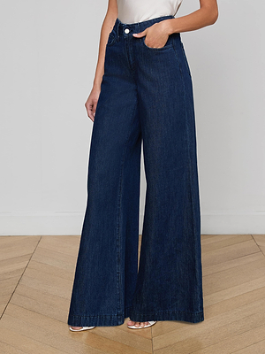 A person in Pacey Wide-Leg Jean (high-rise, wide-leg, dark wash) and a sleeveless white top stands on a wooden floor with hands in pockets. The face is not visible.