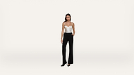 A woman stands against a plain white background, wearing a white strapless top, black high-waisted pants, and black heels.