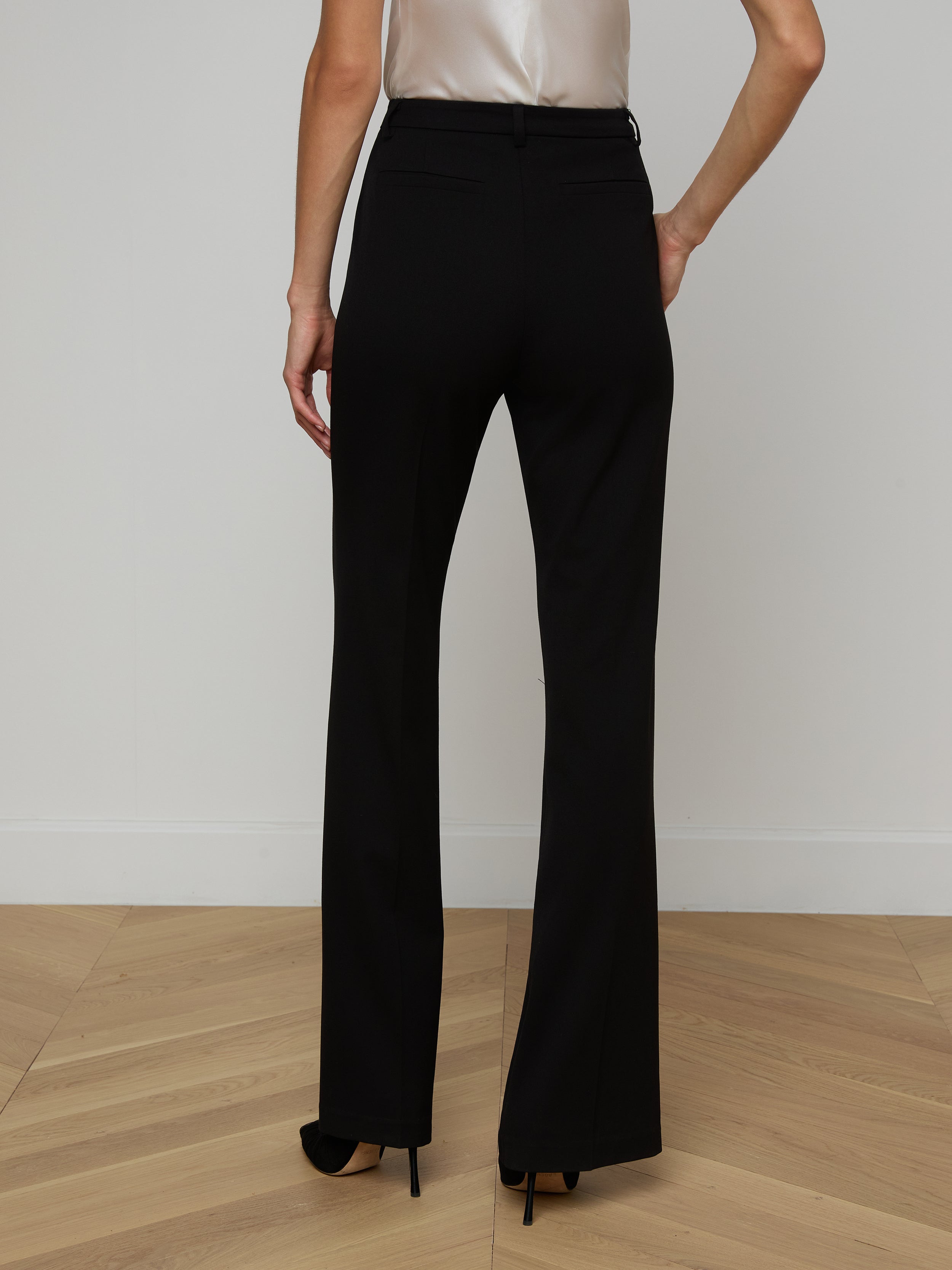 A person wearing the Frances Bootcut Trouser in black with black high heels, seen from behind. The tailored trousers are made from a stretch suit fabric, and the person is standing against a plain, light background.