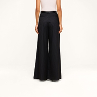 A person shown from the back against a beige background wears a white sleeveless top paired with the Chelsy Wide-Leg Pant, featuring high-waisted, wide-leg pinstripes and a black belt.