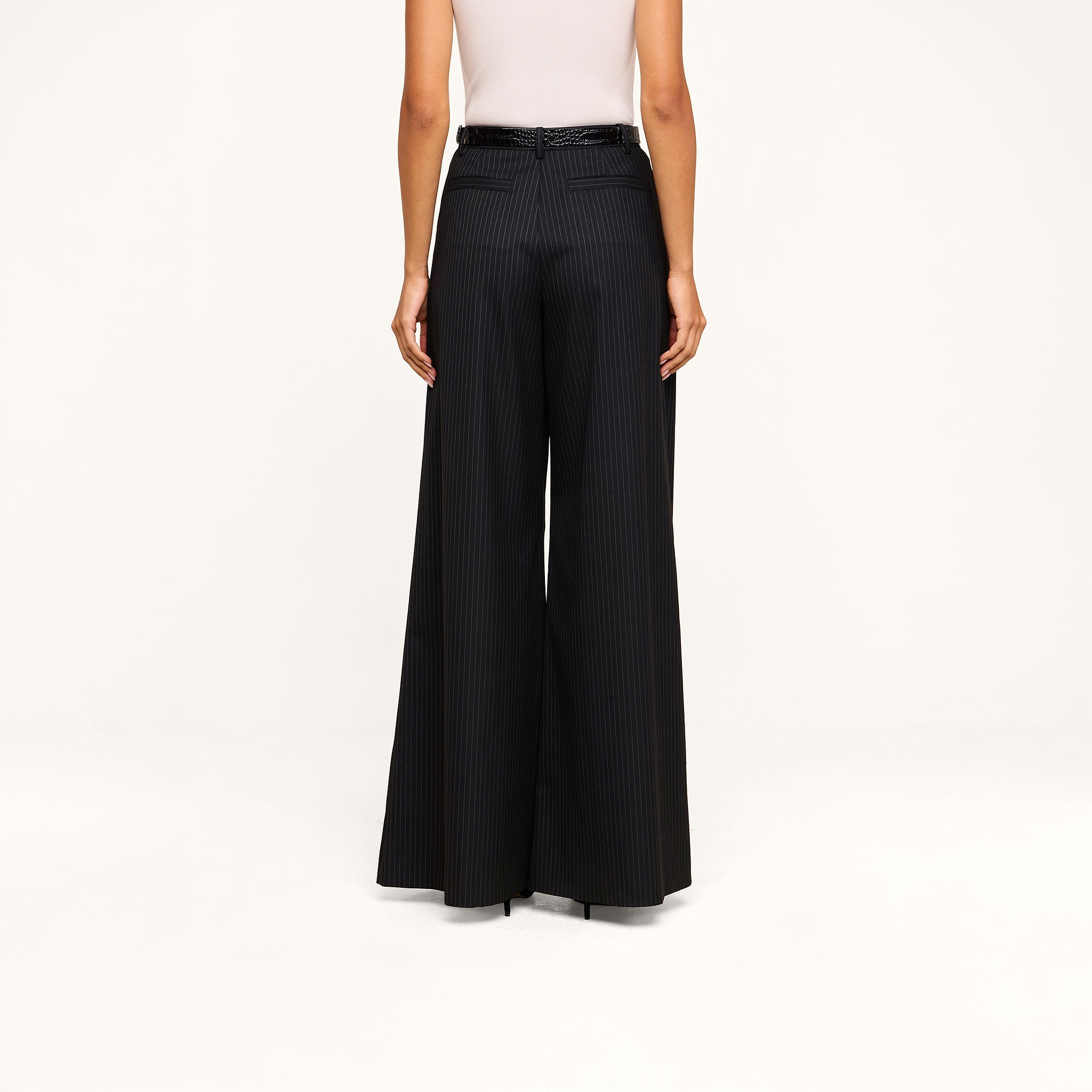 A person shown from the back against a beige background wears a white sleeveless top paired with the Chelsy Wide-Leg Pant, featuring high-waisted, wide-leg pinstripes and a black belt.