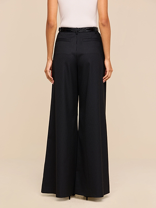 A person shown from the back against a beige background wears a white sleeveless top paired with the Chelsy Wide-Leg Pant, featuring high-waisted, wide-leg pinstripes and a black belt.