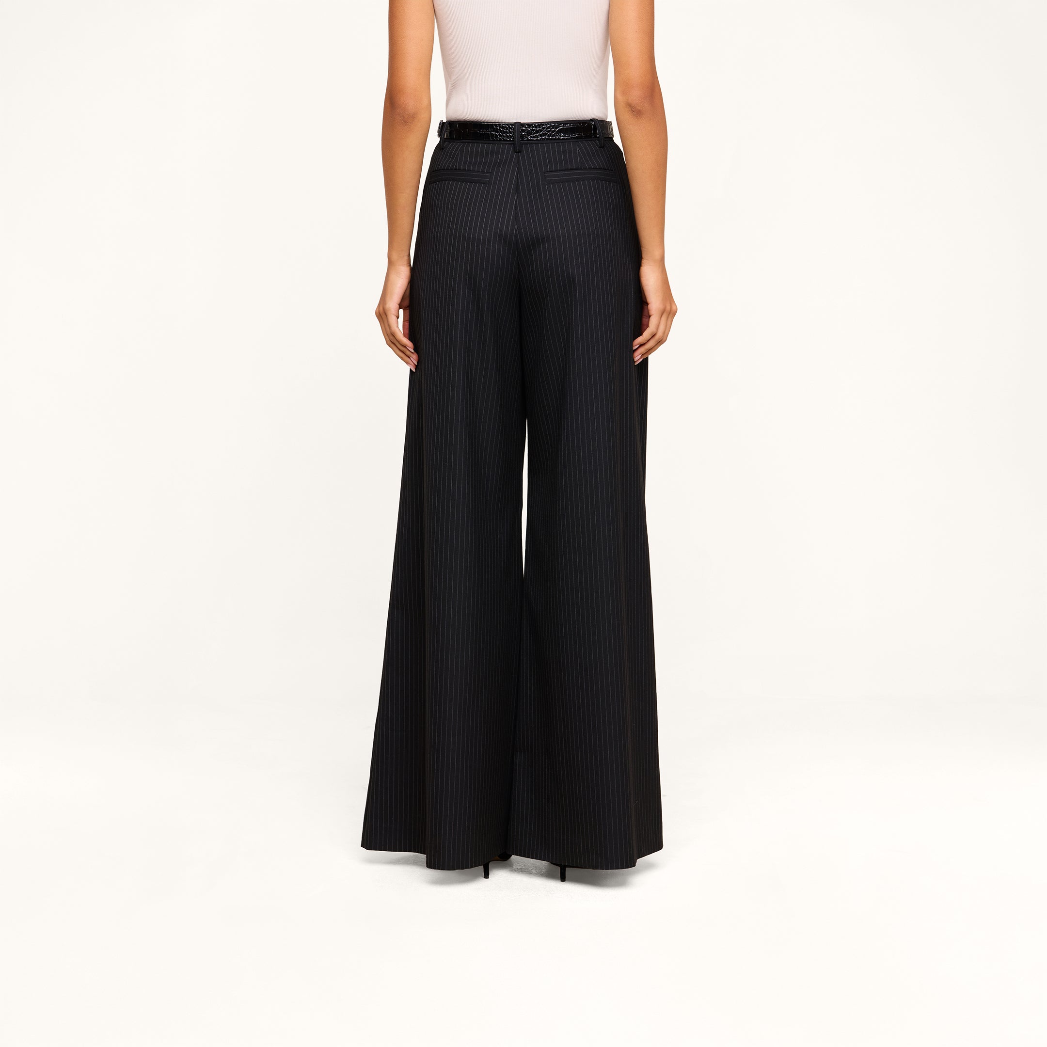 A person shown from the back against a beige background wears a white sleeveless top paired with the Chelsy Wide-Leg Pant, featuring high-waisted, wide-leg pinstripes and a black belt.