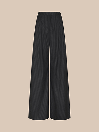 The Chelsy Wide-Leg Pant features a high waist, tailored waistband, and pressed pleats in classic black pinstripe. These wide-leg trousers are showcased against a plain beige background.