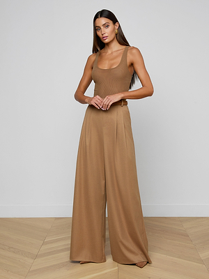 Woman standing indoors against a plain wall, wearing the Chelsy Wide-Leg Pant in suit fabric with a sleeveless, fitted tan top. She has long brown hair down and her arms are relaxed in front of her.