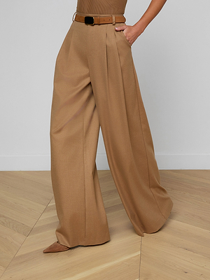 Wearing the Chelsy Wide-Leg Pant, styled with a brown belt and pointed-toe shoes, someone stands on a light wood floor with one hand in their pocket. The image is cropped above the waist.