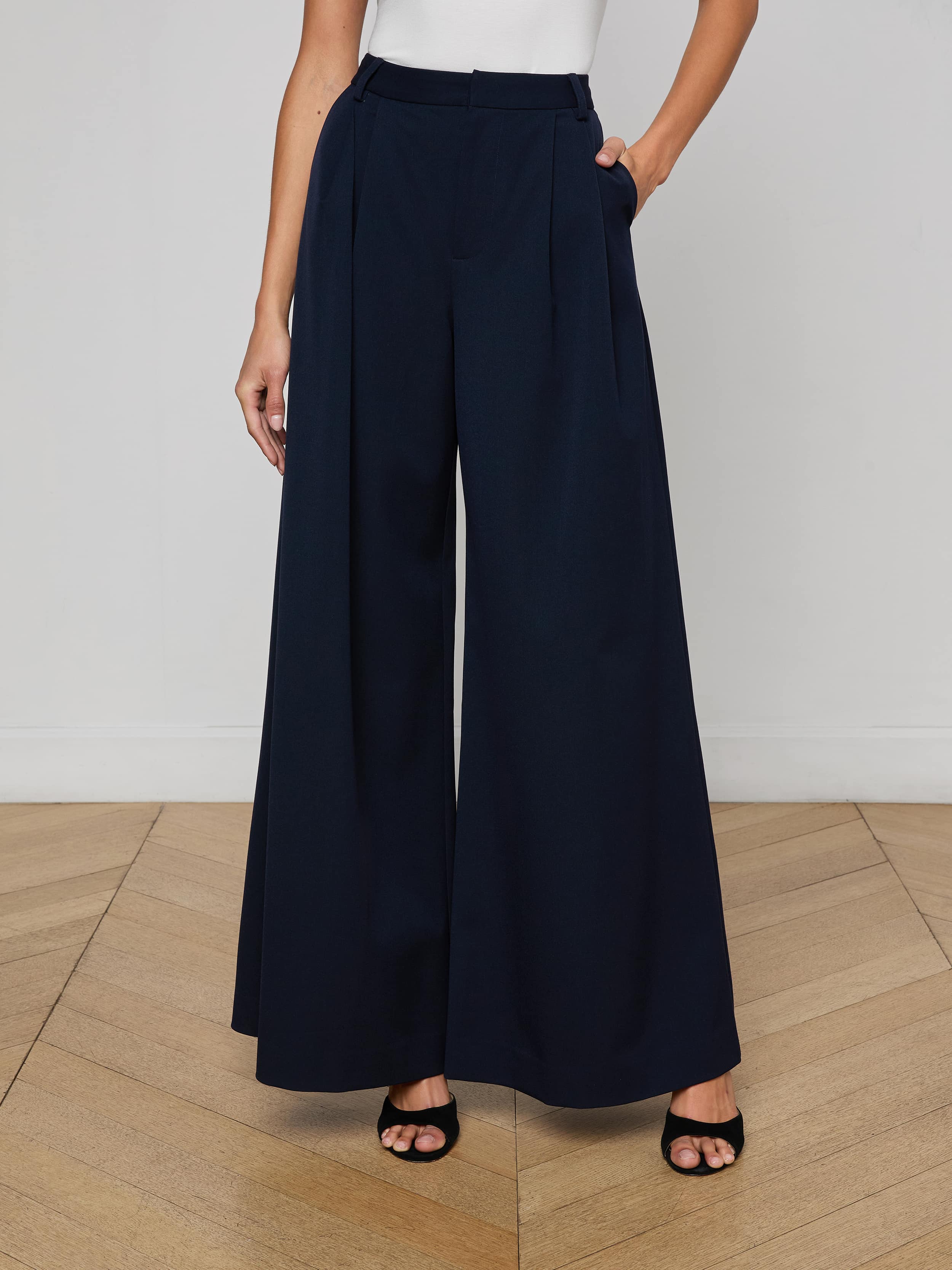 A person wearing a white sleeveless top, the Chelsy Wide-Leg Pant in a high-waisted dark stretch suit fabric, and black open-toe heels stands against a plain light background.