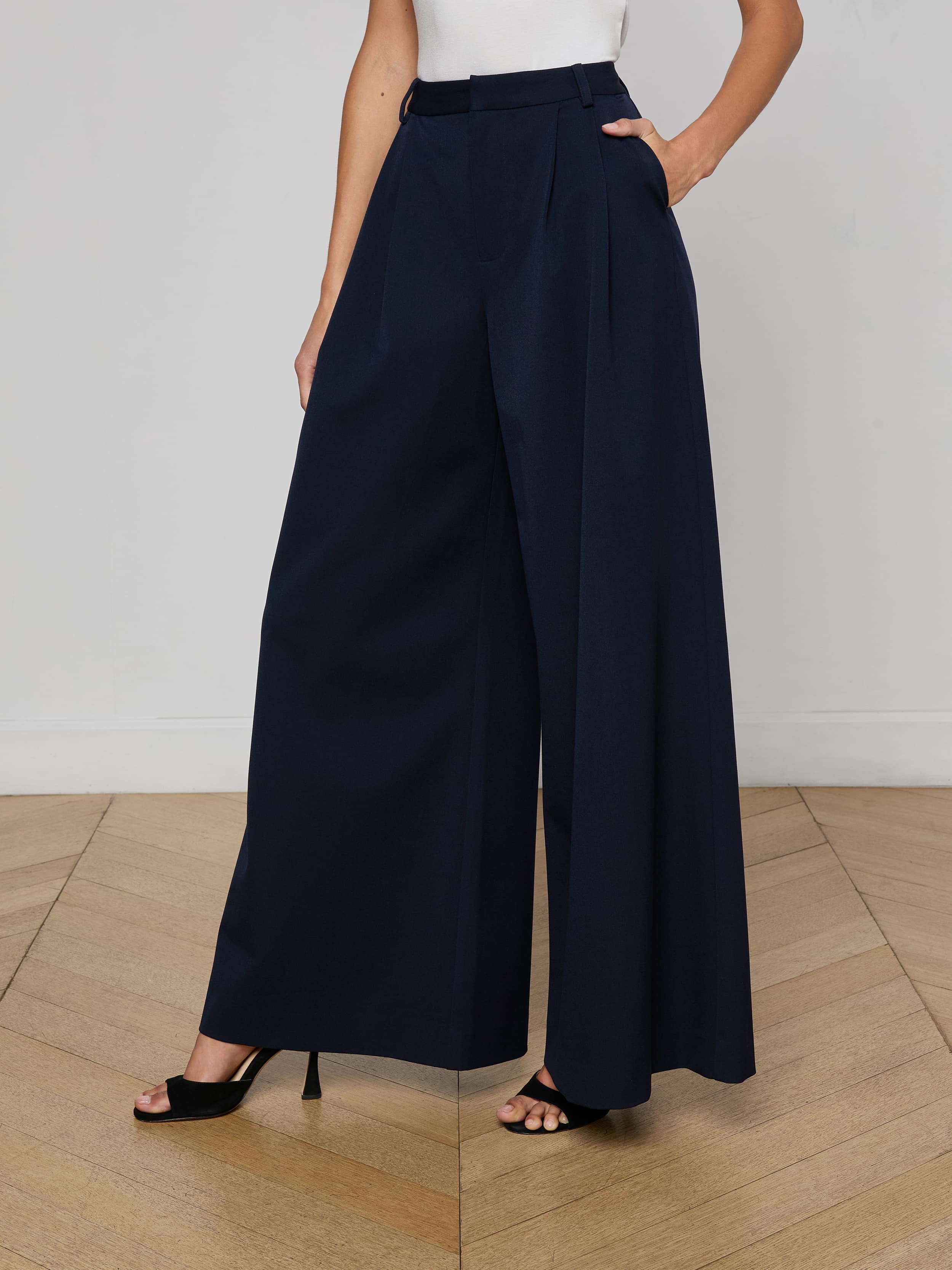 A person is wearing the Chelsy Wide-Leg Pant, made from stretch suit fabric, paired with black open-toe heels. The person is shown from the shoulders down against a plain, light background.