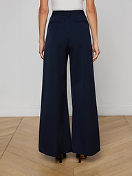 A person wearing a white sleeveless top and the Chelsy Wide-Leg Pant, made from stretch suit fabric, is seen from the back standing against a plain light background.