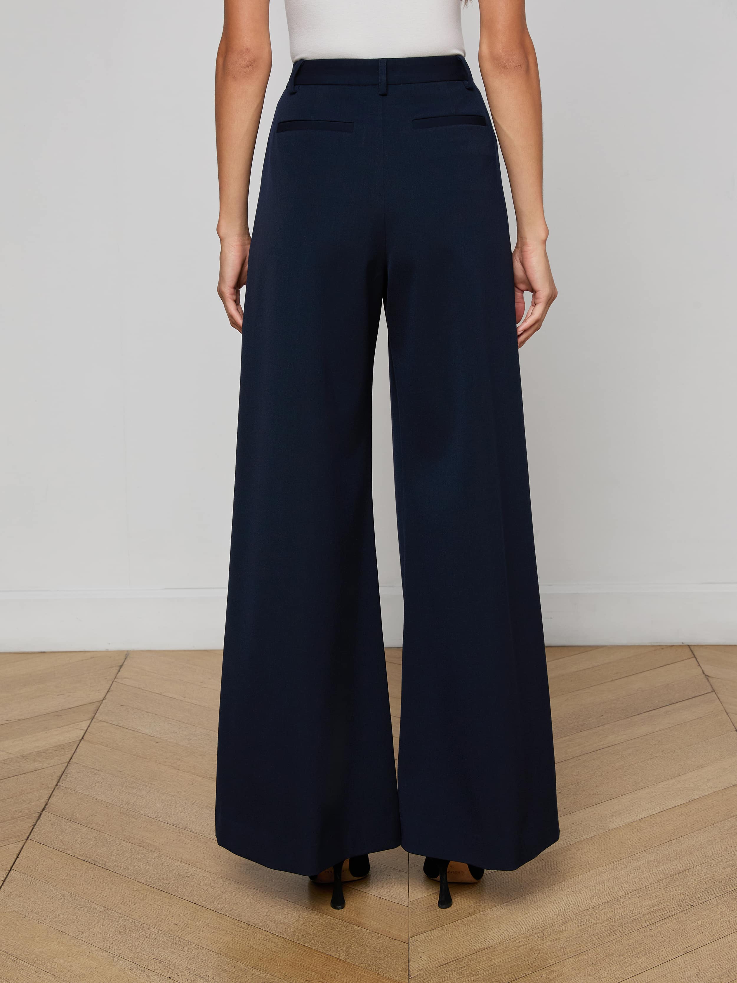 A person wearing a white sleeveless top and the Chelsy Wide-Leg Pant, made from stretch suit fabric, is seen from the back standing against a plain light background.