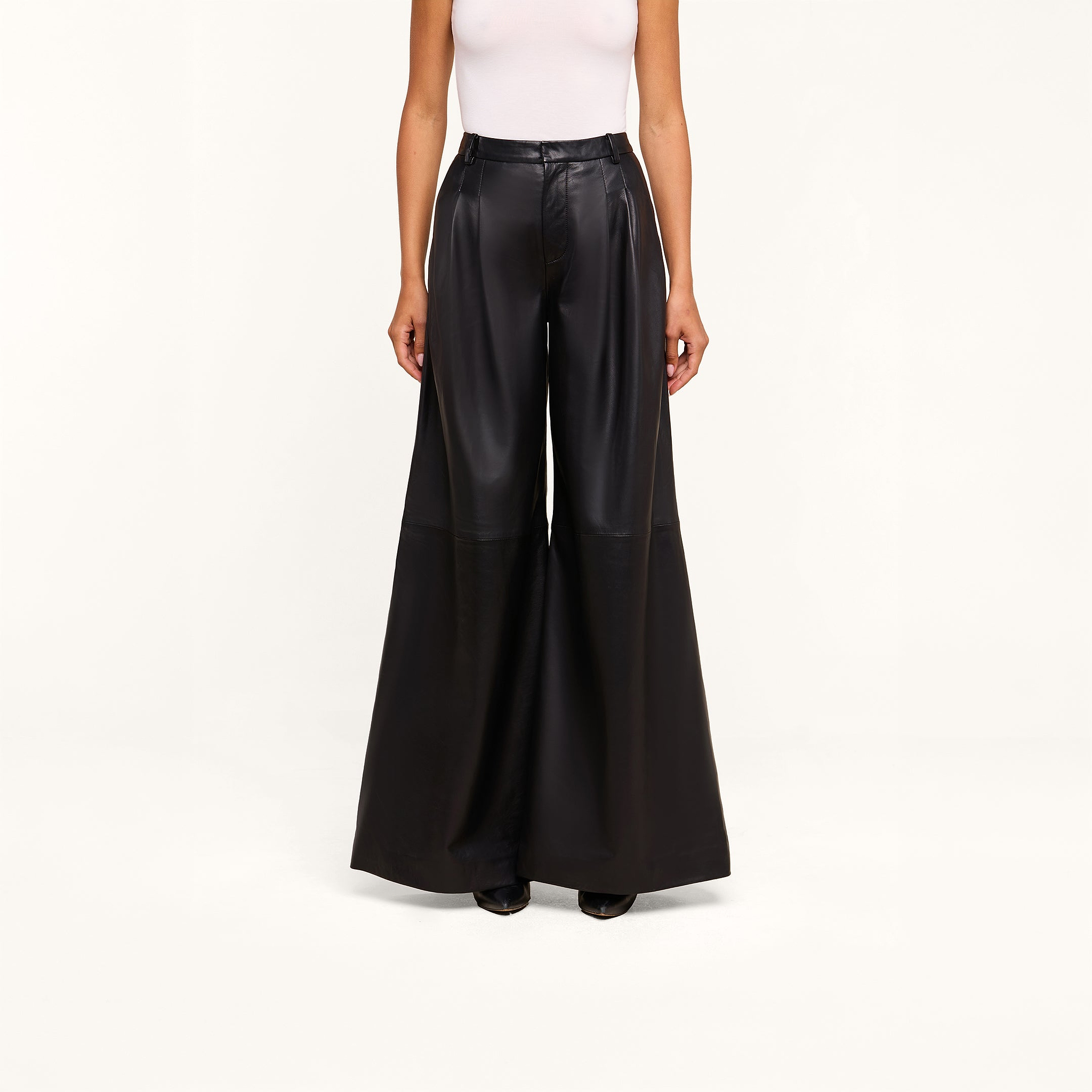 A person wearing a white sleeveless top and the Chelsy Leather Wide-Leg Pant in a high-rise, wide-leg lambskin leather style stands against a plain white background.