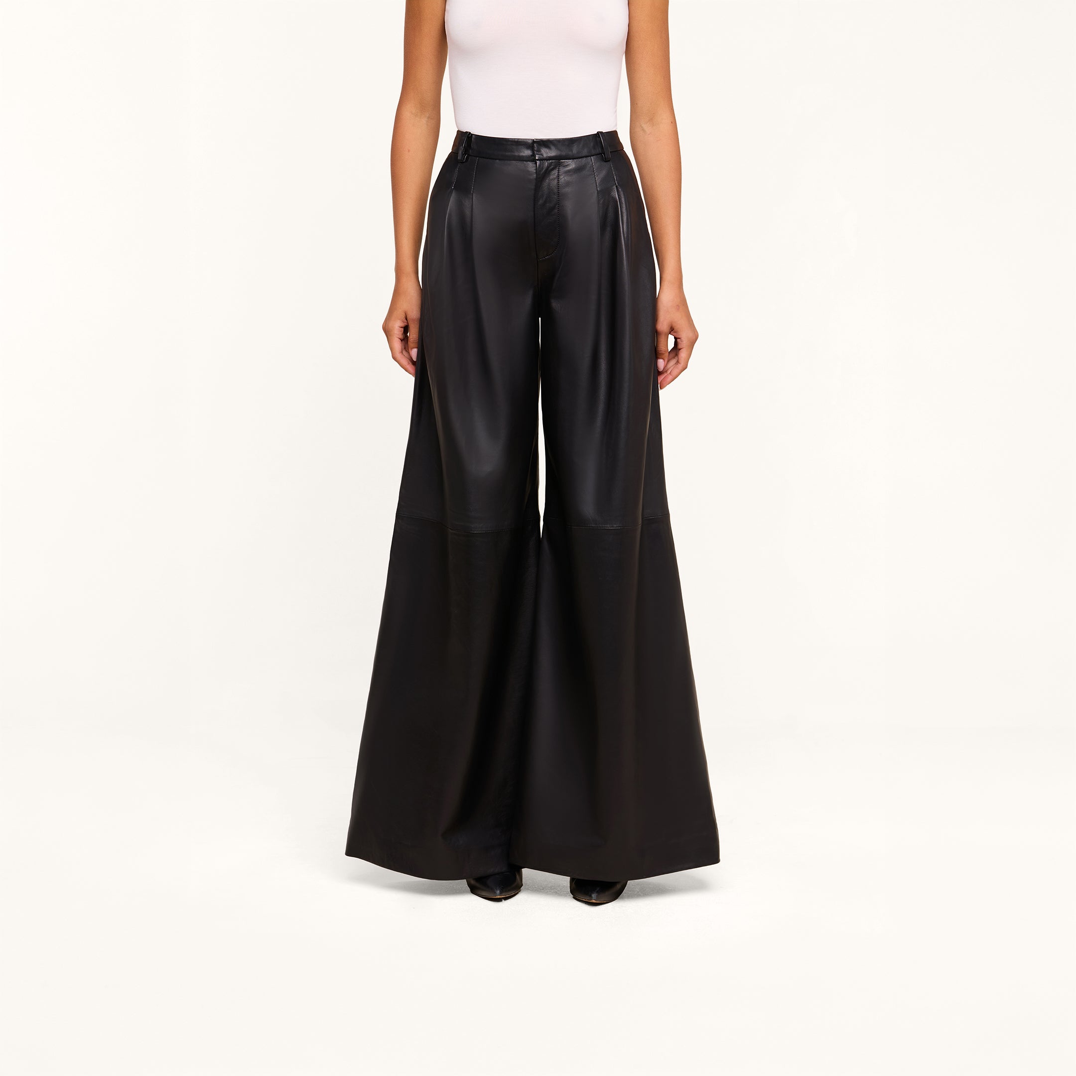A person wearing a white sleeveless top and the Chelsy Leather Wide-Leg Pant in a high-rise, wide-leg lambskin leather style stands against a plain white background.
