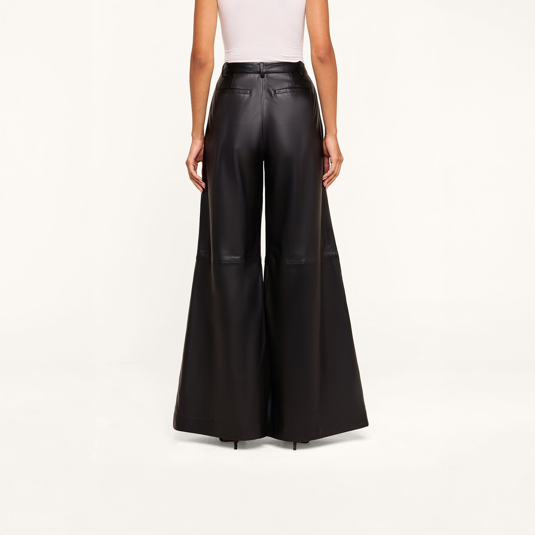 A person is wearing a white sleeveless top and high-rise, black Chelsy Leather Wide-Leg Pants made from lambskin, standing facing away against a plain light background.