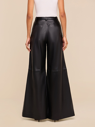 Wearing the Chelsy Leather Wide-Leg Pant in a high-rise, black lightweight leather, paired with a white sleeveless top, a person is pictured from the back against a plain beige background.