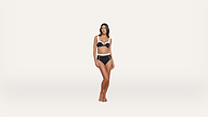 A woman stands barefoot against a plain white background, wearing a navy blue and white bikini set with high-waisted bottoms featuring decorative buttons.