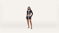A woman stands barefoot, wearing a dark blue, cropped jacket and matching short skirt with white trim and pocket details, against a plain white background.