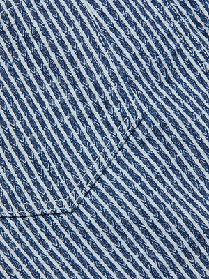 Close-up of the Jolene Mini Skirt's blue and white striped denim, highlighting a pocket with diagonal stitching and a repeating slanted oval pattern.
