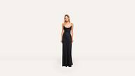 A woman stands against a plain, light background wearing a long, sleeveless black dress with a scoop neckline and minimalist style.