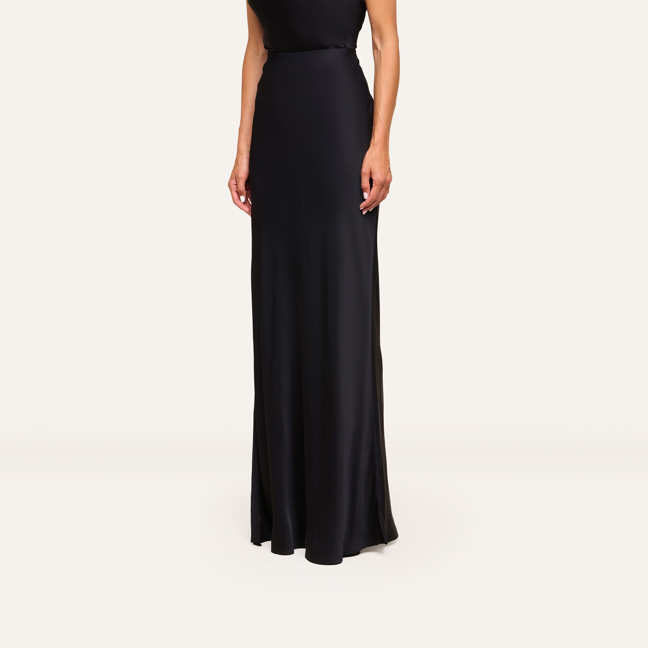 A woman models the Zeta Satin Maxi Skirt, standing against a plain white background with her face out of frame and only her body from the shoulders down visible.