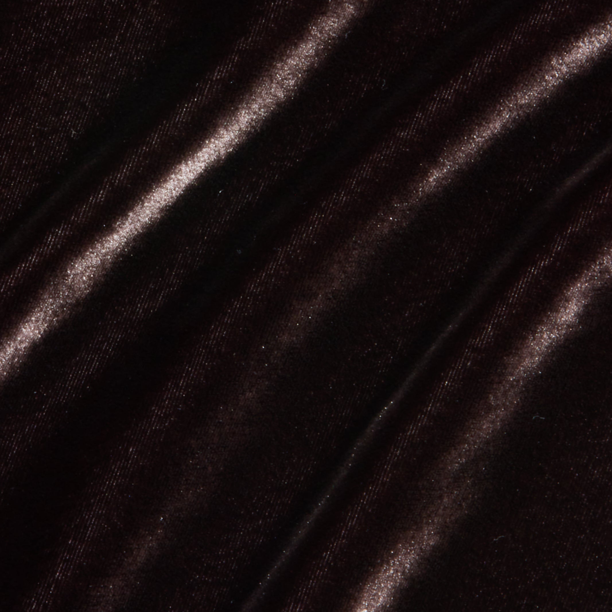 Close-up of dark brown velvet fabric with soft, diagonal folds. Light gently reflects off the plush, smooth surface—perfect for the Zeta Velvet Maxi Skirt or for adding elegant texture to a minimalist wardrobe.
