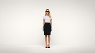 A woman wearing sunglasses, a white top, and a black skirt stands against a plain white background, facing forward with her arms at her sides.