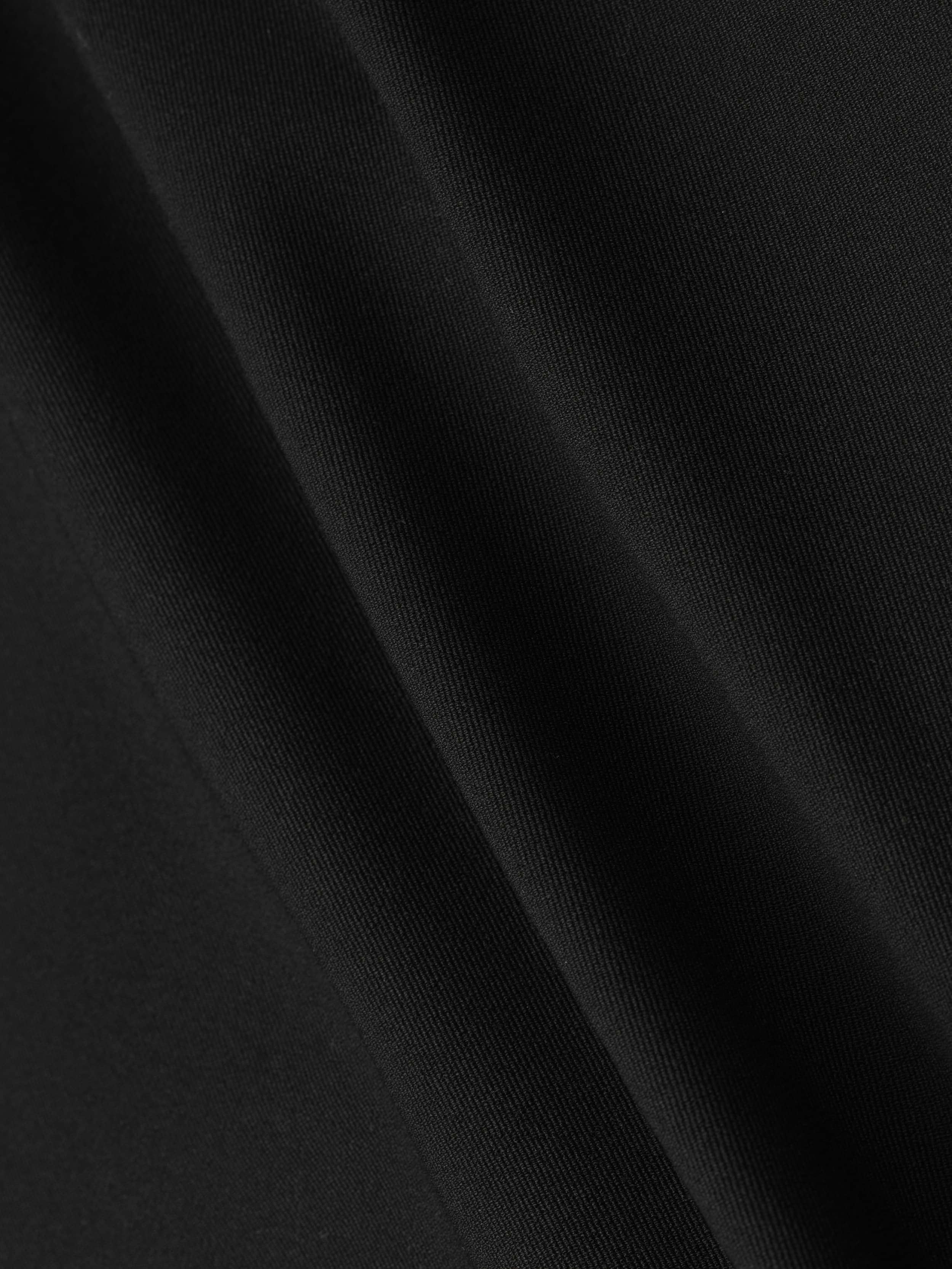 Close-up of smooth black stretch fabric from the Olyvia Pencil Skirt, showing subtle folds and soft shadows that highlight its texture and curve-skimming fit, ideal for a sleek silhouette.