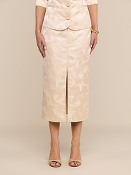 A woman stands facing forward against a plain white background, wearing the Madonna Midi Skirt with a beige butterfly jacquard floral pattern as part of a matching skirt suit. Her hands rest relaxed at her sides, and she accessorizes with open-toed heels and a bracelet.