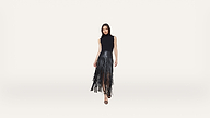 Woman standing and posing in a sleeveless black top and a black fringe skirt with high heels, against a plain white background.