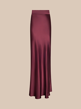 The Ryker Silk Maxi Skirt is a long, high-waisted skirt in a rich merlot red hue with a subtle sheen, crafted from bias-cut silk that flares gracefully at the hem, shown against a simple beige background.