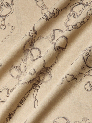 Close-up of the Ryker Silk Maxi Skirt: beige silk with a subtle sheen, adorned with a dark brown horsebit chain print and soft draping—effortlessly minimalist and sophisticated.