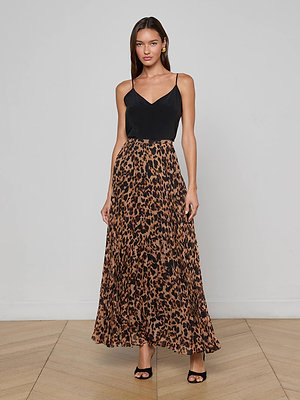 A woman with long hair and a neutral expression wears the L'AGENCE Torin Pleated Maxi Skirt in leopard print poly chiffon, paired with a black sleeveless top and black heeled sandals, standing against a plain background.