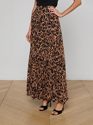 A person wears a black top, the L'AGENCE Torin Pleated Maxi Skirt in leopard print poly chiffon, and black high-heeled sandals, standing against a plain background on a wooden floor.