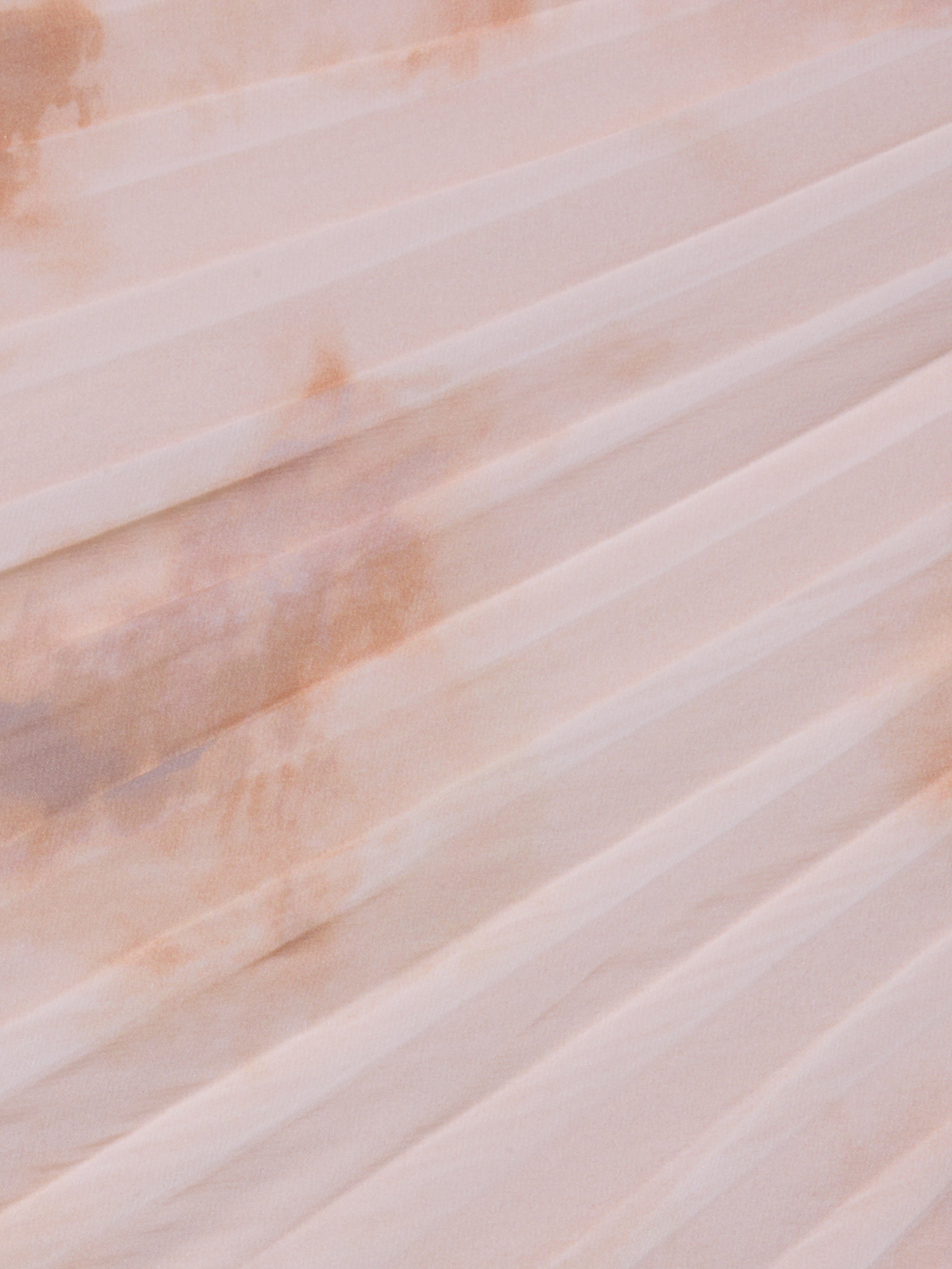 A close-up of the Torin Pleated Maxi Skirt’s light pink poly chiffon fabric, featuring pleats and a faint brownish stain across the folds.