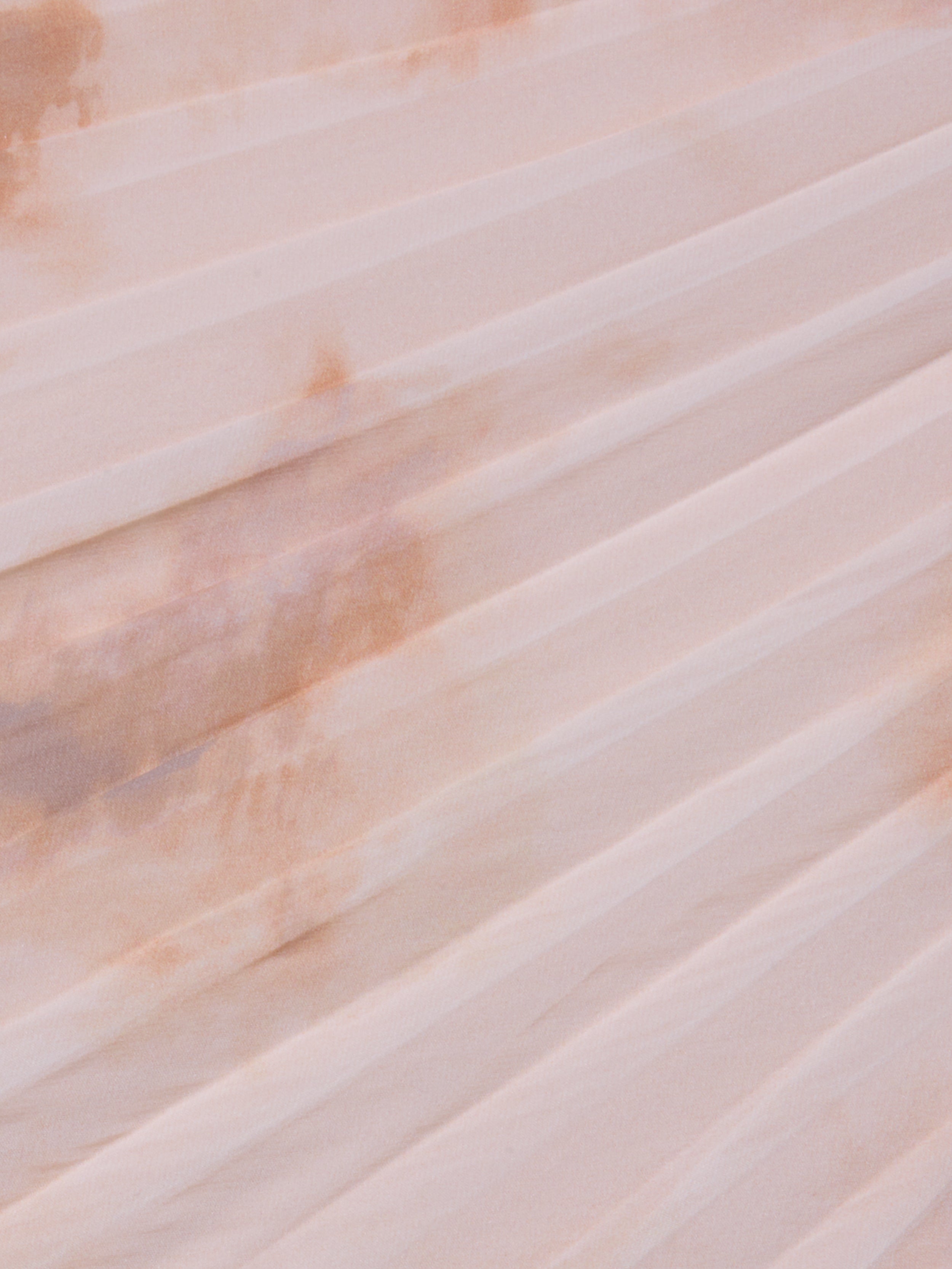 A close-up of the Torin Pleated Maxi Skirt’s light pink poly chiffon fabric, featuring pleats and a faint brownish stain across the folds.