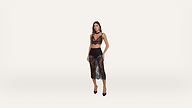 A woman stands against a plain white background, wearing a black lace bralette, a matching sheer lace skirt, black underwear, and black high heels.