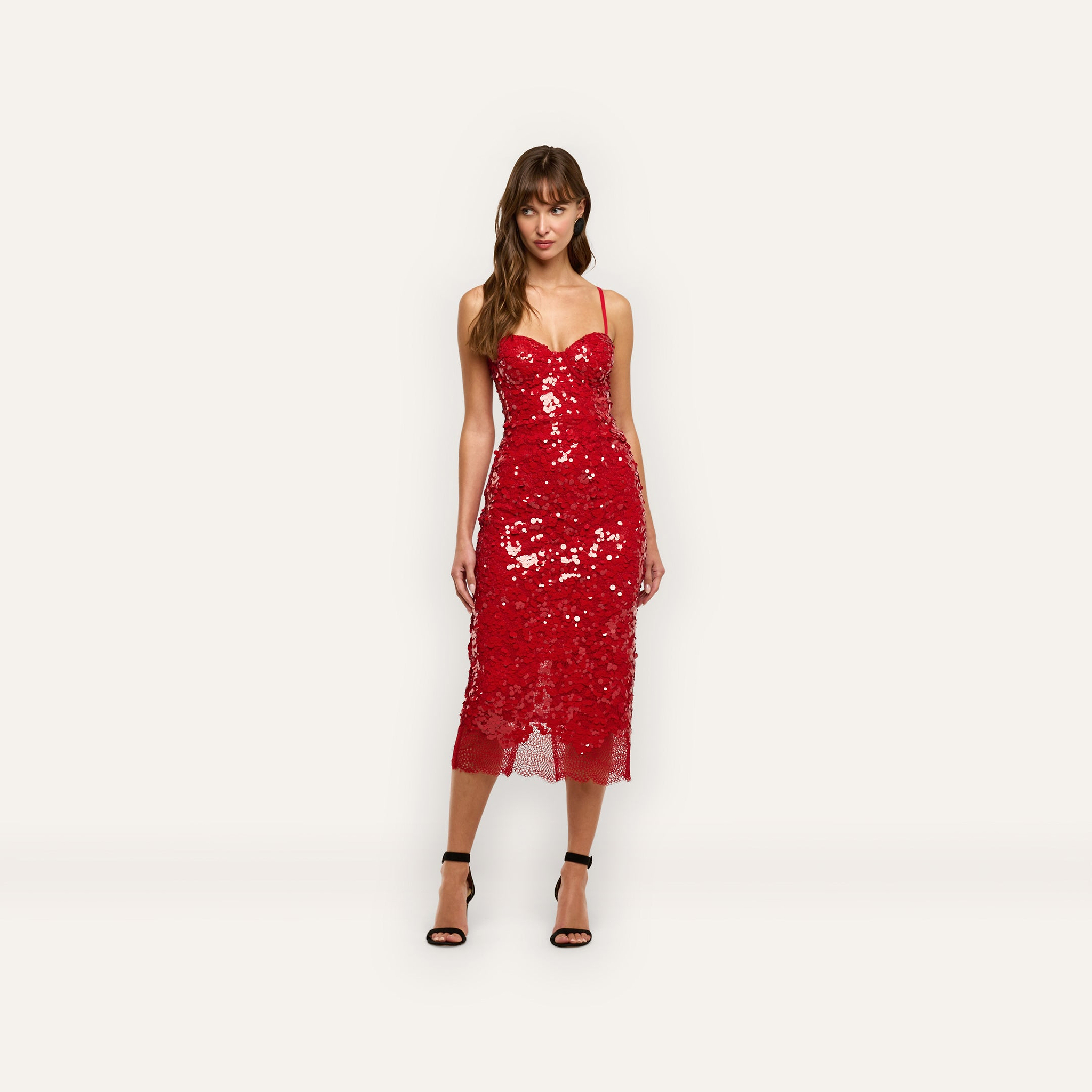 A woman wearing a red sequined Makena Sequin Pencil Skirt midi party dress with thin straps and black heeled sandals.